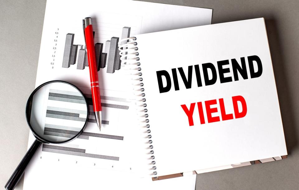 The words Dividend Yield in a notebook sitting on top of paper with a graph on it and a magnifying glass.